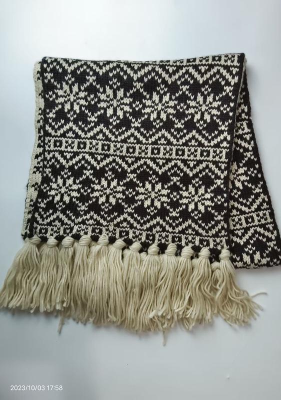 Folded black and cream Fair Isle knitted scarf with geometric snowflake pattern and long cream tassel fringe along bottom edge