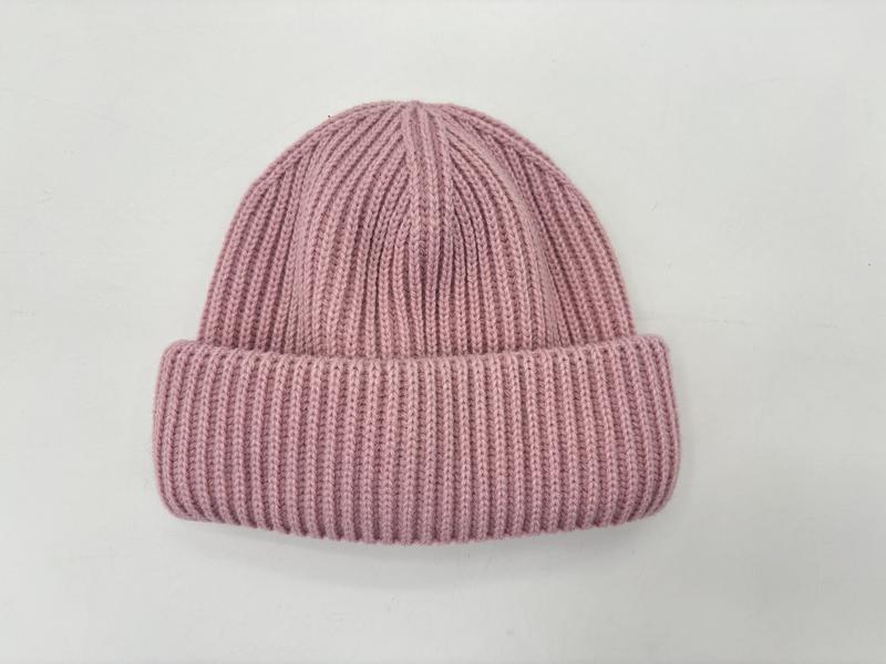 Flat lay of a dusty pink ribbed knit winter beanie hat with a rolled cuff, photographed on a white background