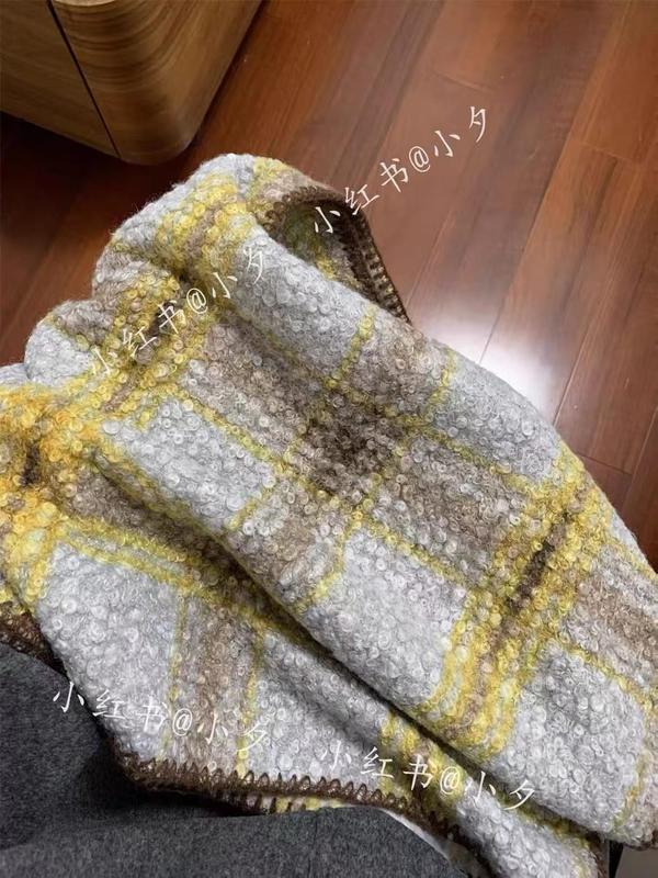 Folded chunky boucle plaid throw blanket in gray, yellow, and beige tones resting on a chair with wood floor background
