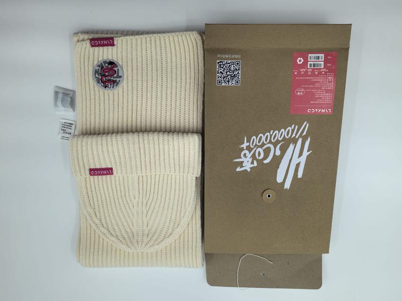 Cream ribbed knit beanie hat and matching scarf set with burgundy logo patch displayed beside kraft paper gift box packaging