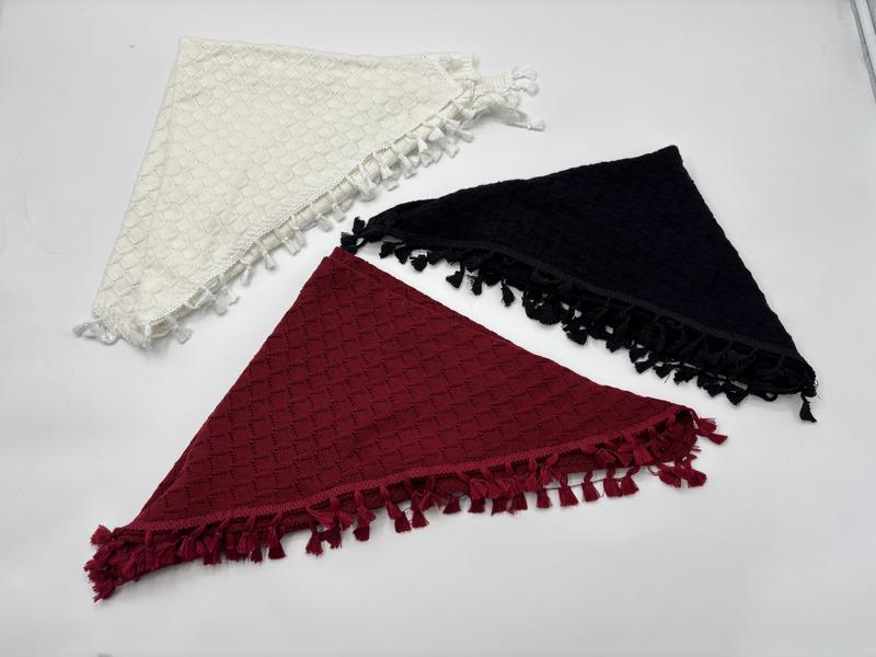 Three triangle knit shawls with tassel fringe in cream, black, and burgundy laid flat on white background