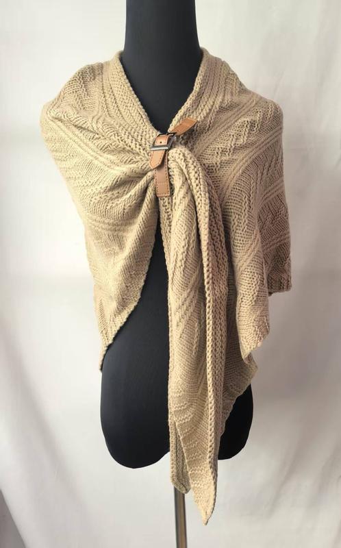Beige cable knit wrap shawl secured with tan leather buckle clasp displayed on black mannequin torso
