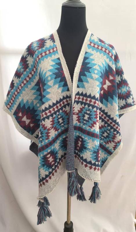 Open-front knitted wrap poncho with Aztec geometric pattern in teal, burgundy, navy, and cream with tassel fringe hem on mannequin