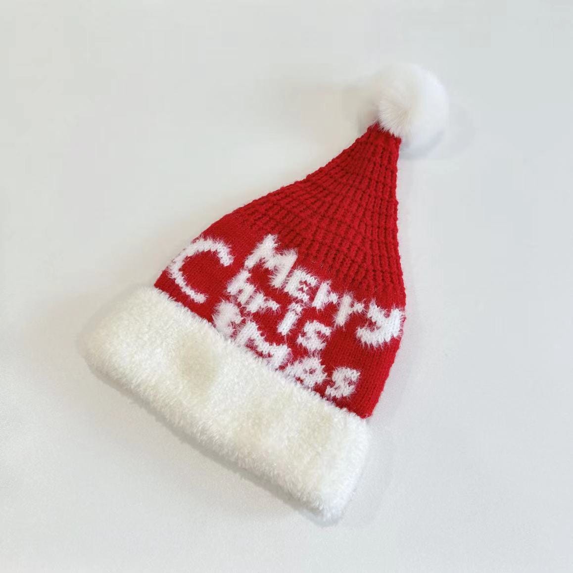 Red knitted Santa Claus hat with white fluffy fur brim, Merry Christmas text pattern, and white pom-pom on top