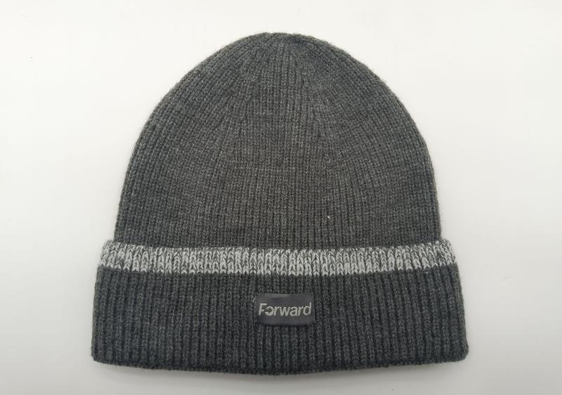 Charcoal grey ribbed knit beanie hat with light grey stripe on folded cuff and small label patch, laid flat on white background