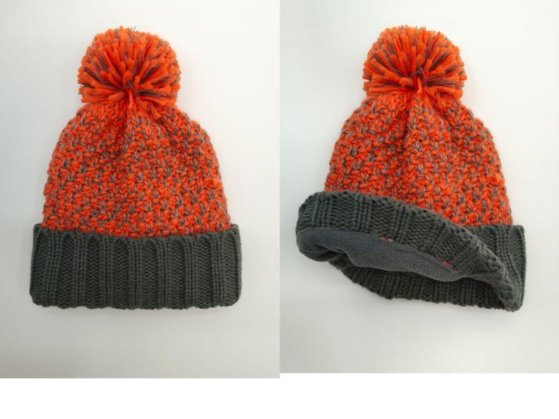 Orange and gray two-tone chunky knit winter beanie hat with large pom pom and folded gray ribbed cuff, fleece-lined interior shown