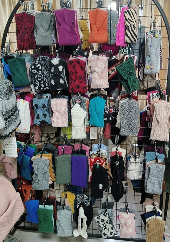 Large retail display rack featuring dozens of knitted fingerless gloves and mittens in various colors, patterns, and textures for winter