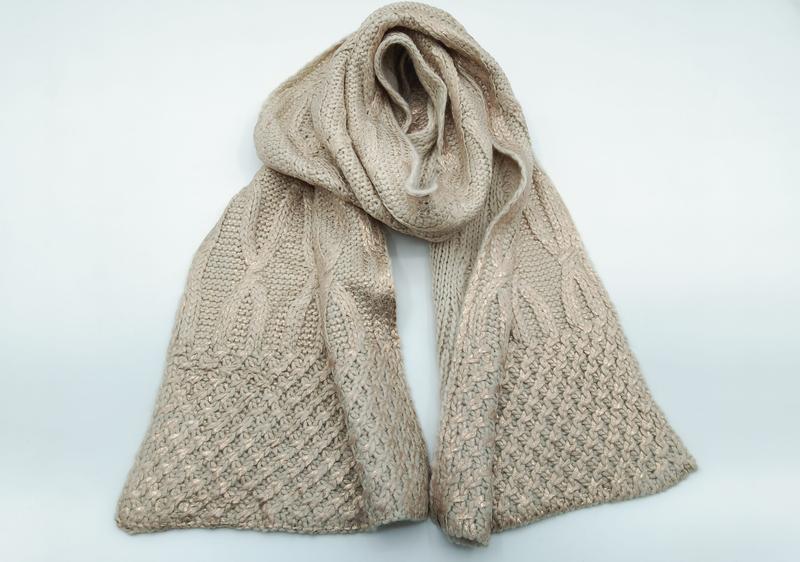 Beige chunky cable knit scarf with gold metallic thread shimmer, looped and draped flat on white background