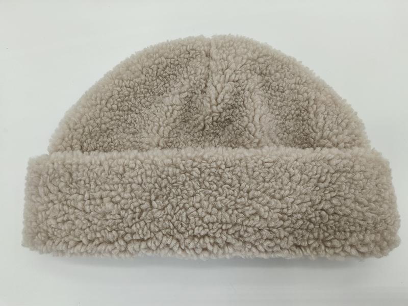 Beige sherpa fleece cuffed beanie hat with textured curly pile fabric and folded brim on white background