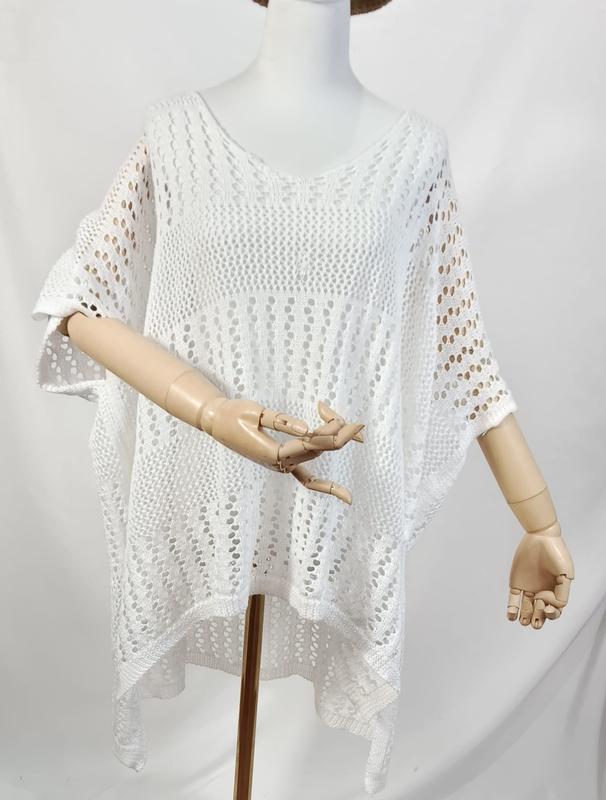 White oversized open-knit crochet poncho top with V-neck and short sleeves displayed on a mannequin with wooden hands