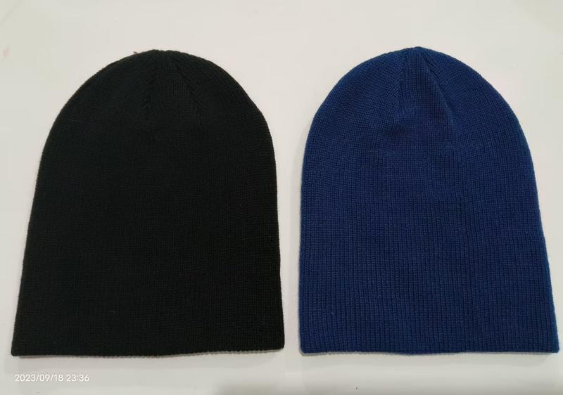 Two plain knit beanie hats laid flat, one black and one royal blue, showing ribbed texture and slouchy style