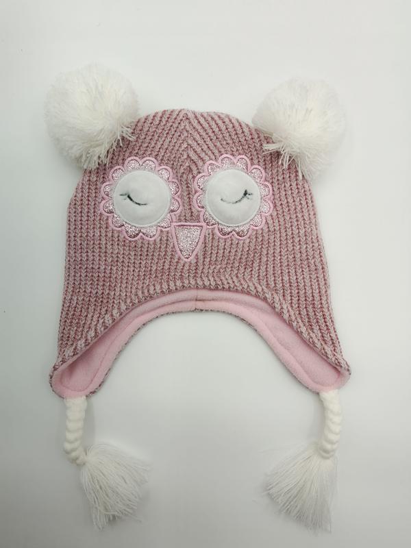 Pink chunky knit children's winter hat with owl face embroidery, white pom poms, ear flaps, and braided tassels