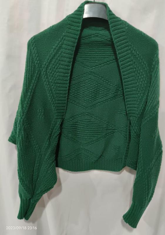 Green chunky knit open front shrug cardigan with diamond cable pattern displayed on hanger, long sleeves with ribbed cuffs