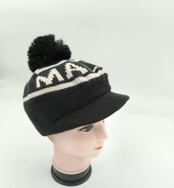 Black knitted pom-pom beanie with brim visor and bold white letter jacquard pattern displayed on mannequin head