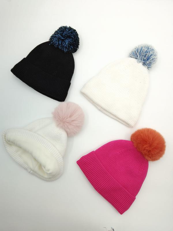 Four ribbed knit winter beanies with colorful pom poms in black, white, and fuchsia pink laid flat on white background