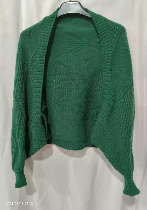 Green open-front knitted cardigan with diamond lace pattern and ribbed cuffs displayed on a hanger against white background