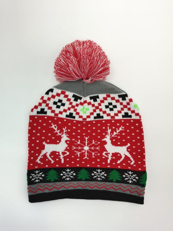 Red holiday knit beanie with white reindeer, snowflakes, green Christmas trees, black geometric pattern, and large red pom-pom on top