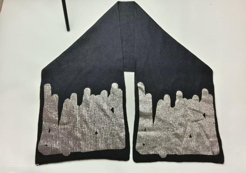 Black ribbed knit scarf laid flat showing both ends with large metallic silver drip or melt pattern print on dark fabric