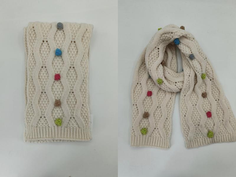 Cream cable knit scarf with colorful bobble details shown folded and draped, featuring blue, pink, green, and tan yarn knots