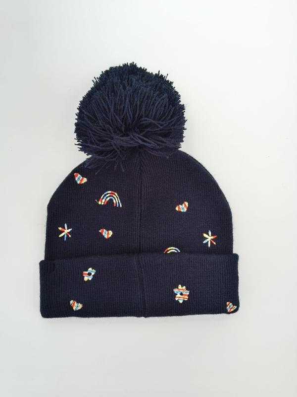 Navy blue ribbed knit winter beanie with large pom-pom and colorful embroidered rainbows, hearts, stars and flowers