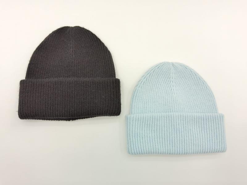 Two ribbed knit cuffed beanie hats laid flat, one charcoal grey and one light blue, on white background