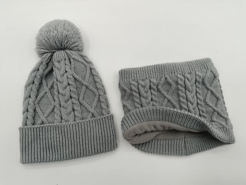Grey cable knit winter beanie hat with pom pom and matching fleece-lined neck gaiter set on white background