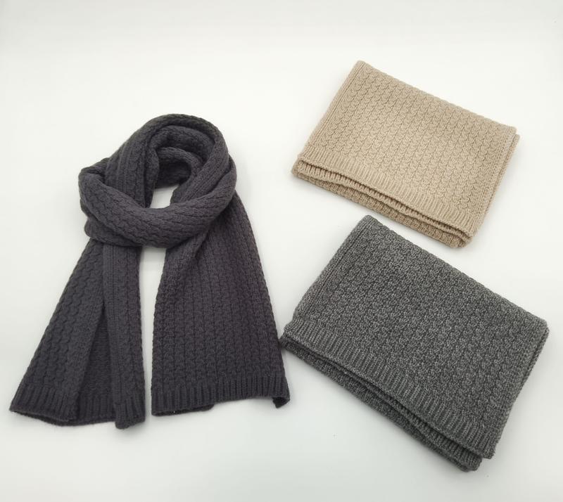 Three cable knit scarves in charcoal, light gray, and beige – one draped open, two folded, on white background