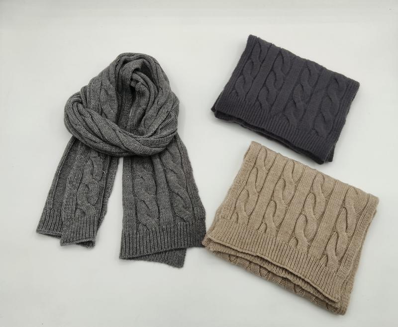 Three cable knit scarves in gray, dark charcoal, and beige folded and displayed flat on white background