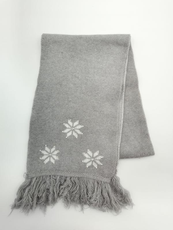 Folded grey knitted throw blanket with white intarsia snowflake motifs and fringe trim on white background