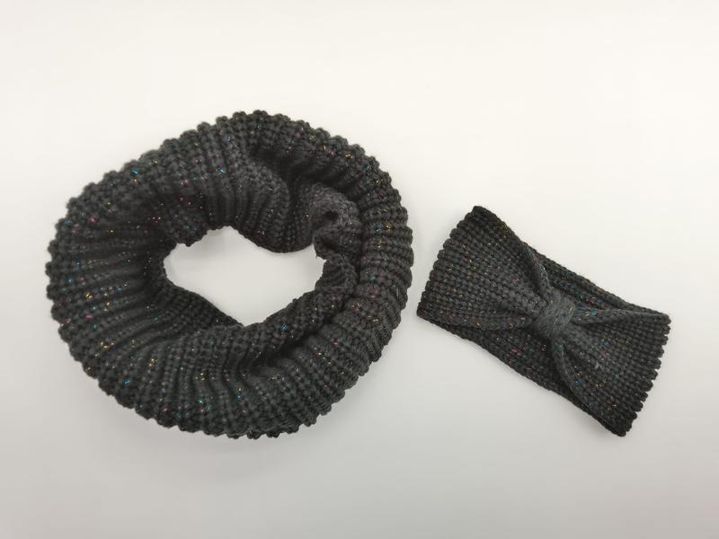Dark gray chunky knit infinity scarf coiled in circle beside matching bow headband with colorful metallic lurex threading