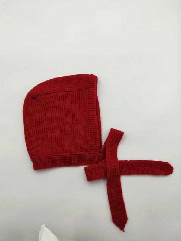 Red ribbed knit baby bonnet with chin tie strings laid flat on white background, handmade crochet infant cap
