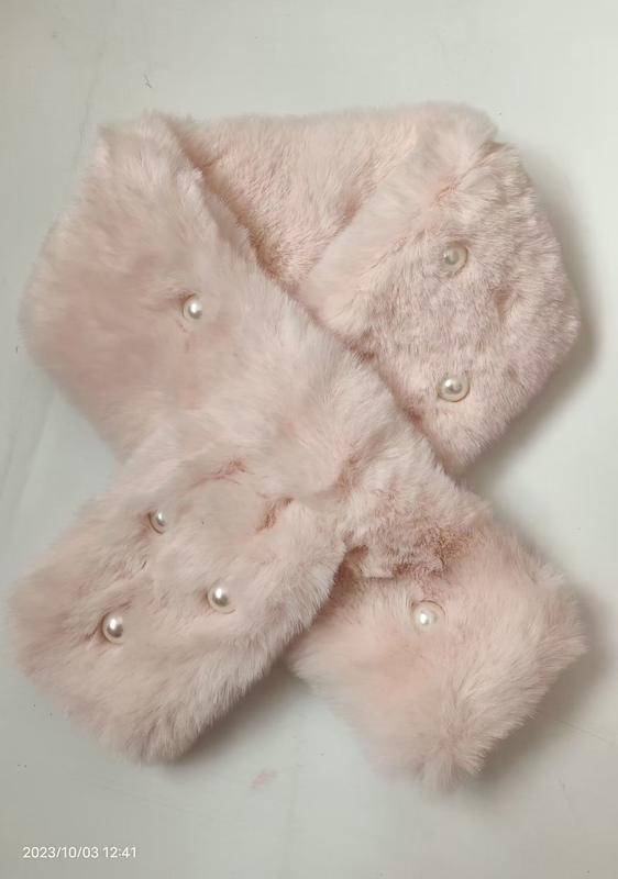 Soft blush pink faux fur crossover neck scarf with decorative pearl buttons laid flat on white surface
