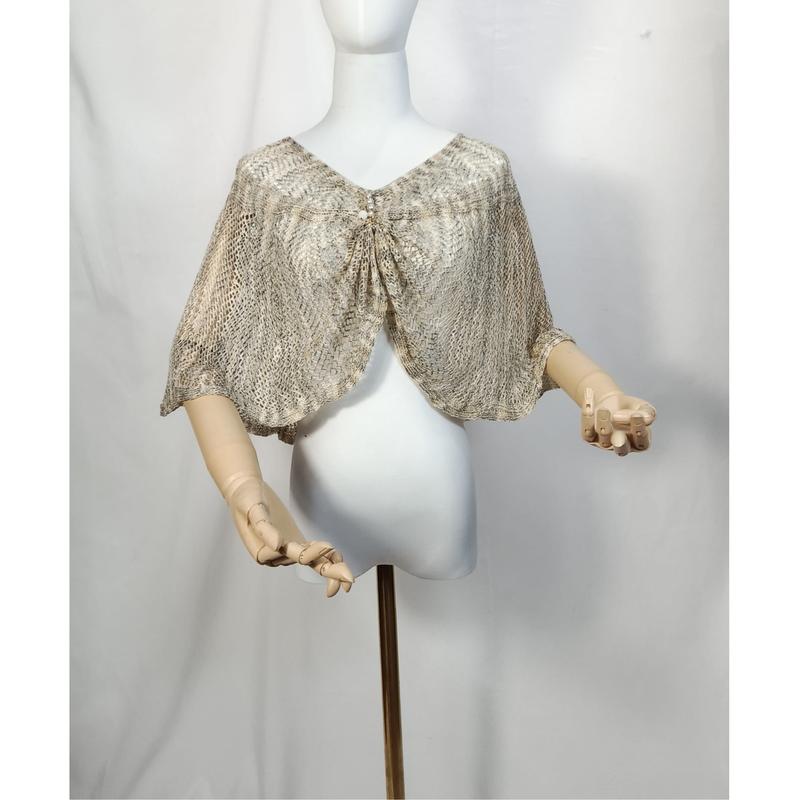 Beige and gold open-knit lace capelet shawl with tie front closure displayed on white mannequin with wooden arms