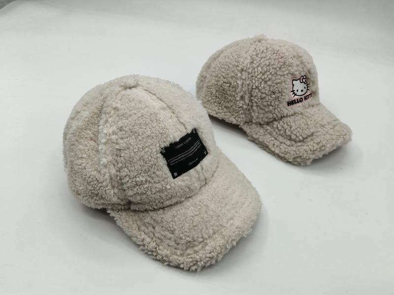 Two cream sherpa fleece baseball caps side by side, one with a black label patch and one with Hello Kitty embroidery on white background