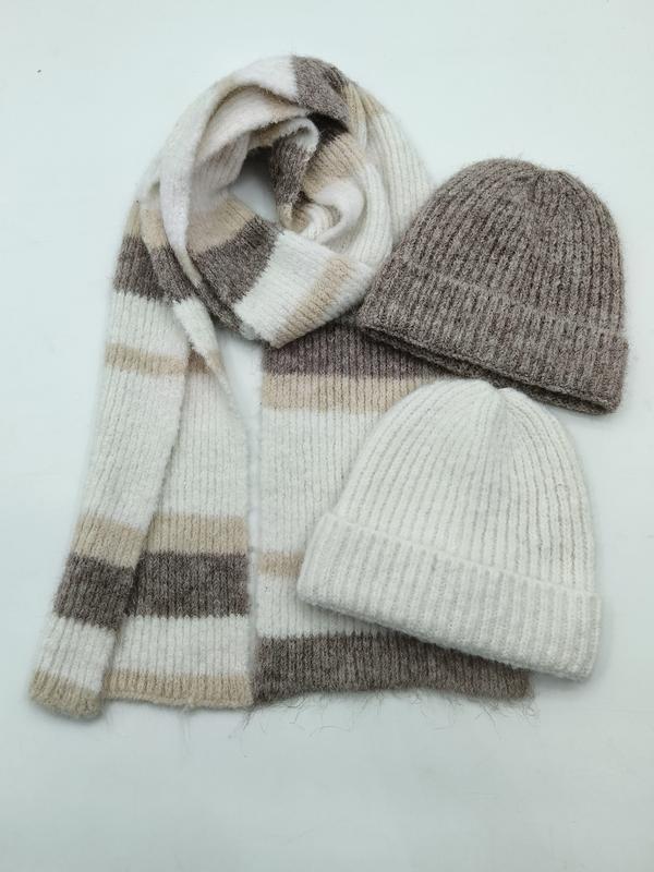 Flat lay of a striped knit scarf in cream, beige and taupe with two ribbed wool beanies in grey and ivory