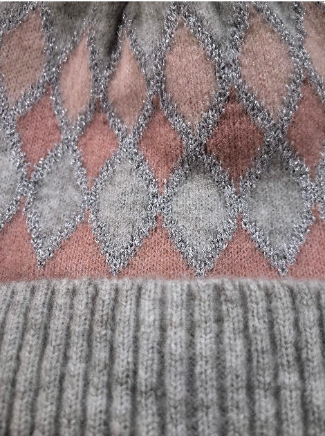 Close-up of a knit beanie showing pink and grey argyle diamond pattern with silver metallic yarn detail and ribbed grey cuff
