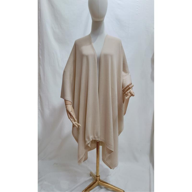 Beige oversized open-front knit wrap poncho cape draped on a mannequin, soft neutral tone with ribbed hem detail