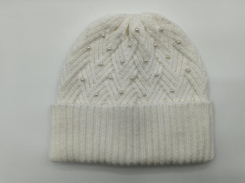 Cream white chunky knit beanie hat with zigzag chevron pattern and scattered pearl bead embellishments on grey background