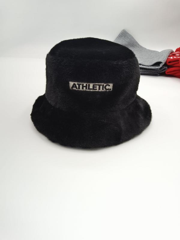 Black fluffy faux fur bucket hat with embroidered Athletic patch label, displayed on white surface with grey and red accessories