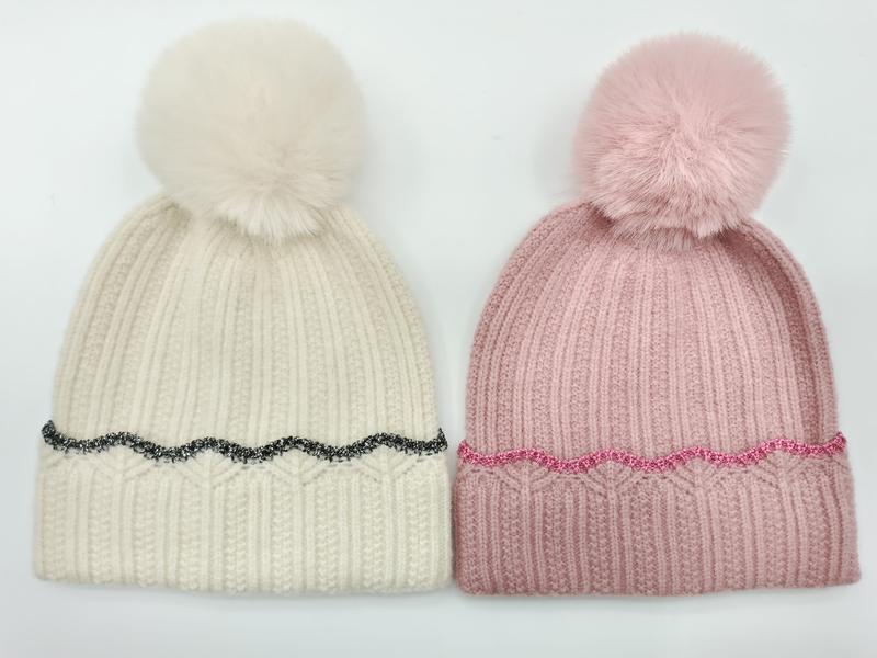 Two ribbed knit pom pom beanies side by side, cream with black glitter trim and pink with pink glitter trim, faux fur pompoms