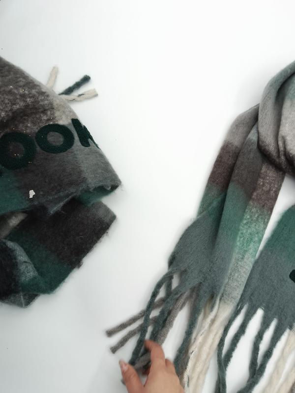 Two green grey and brown plaid wool blend scarves with fringed ends laid flat on white surface, one folded and one unfolded