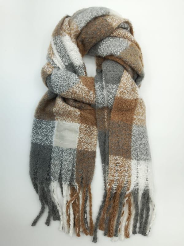 Cozy oversized plaid scarf in grey, camel brown, and white with fringe ends, loosely looped on white background