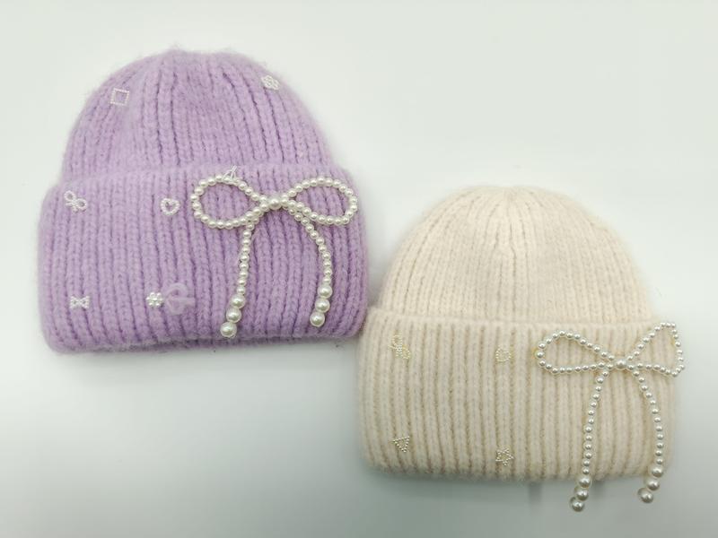 Two chunky knit beanies in lavender and cream with pearl bow embellishments and small embroidered icons on a white background