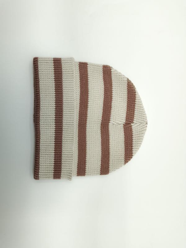 Flat lay of a cream and brown striped ribbed knit beanie hat folded on a white background