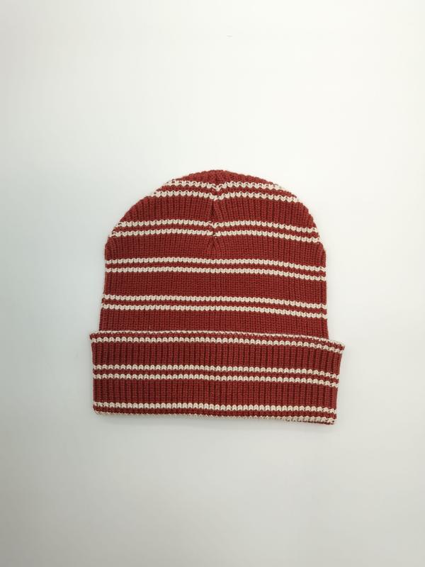 Flat lay of a rust red and cream horizontally striped ribbed knit beanie hat with folded cuff on white background