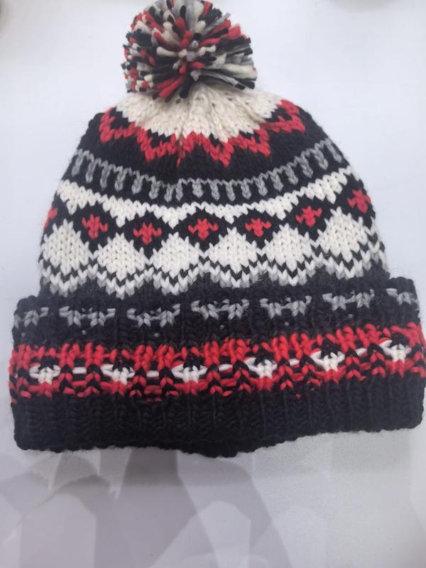 Handknitted Fair Isle winter beanie hat in black, red, white and grey with multicolor pom pom on top