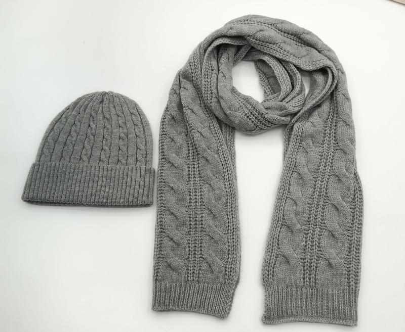 Grey cable knit matching winter beanie hat and long scarf set laid flat on white background