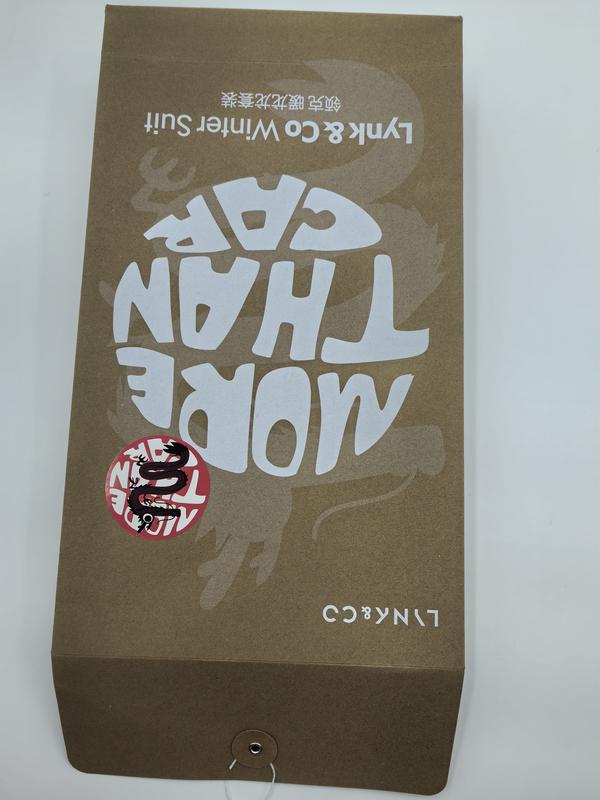 Převrácená dárková krabička z kraft hnědé lepenky s potiskem „More Than Core", dekorativní nálepkou draka a logem Lynk & Co W. Tučná typografie zvýrazňuje moderní streetwear styl. Robustní papírové balení v přírodní hnědé barvě vhodné pro velkoobchod